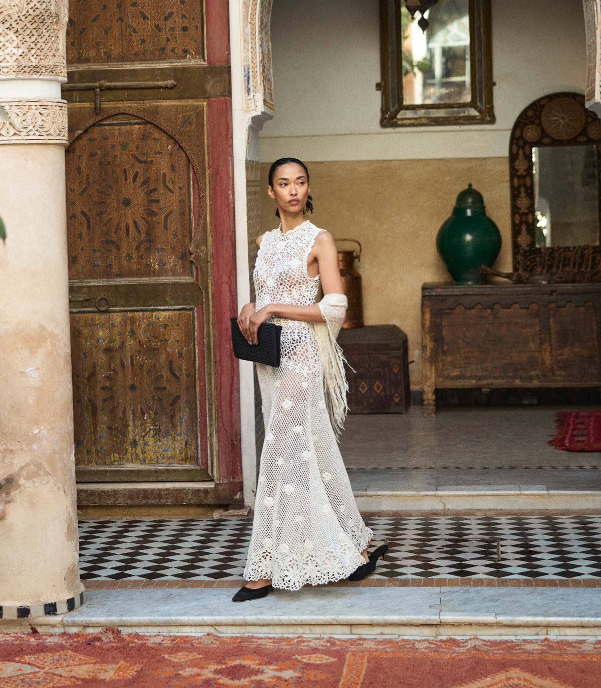 Woman in a white crochet dress standing in an ornate room with decorative elements.