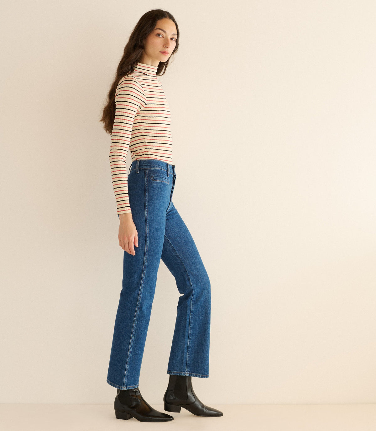 Woman wearing a striped long-sleeve top and blue jeans against a beige background