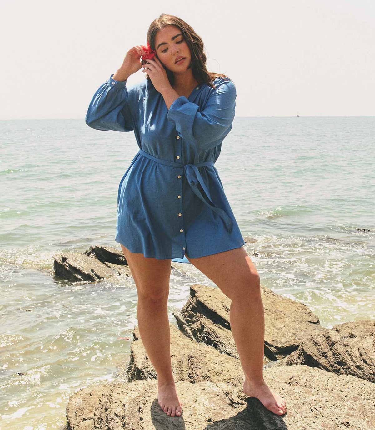 Woman in a blue dress standing on a rock by the ocean
