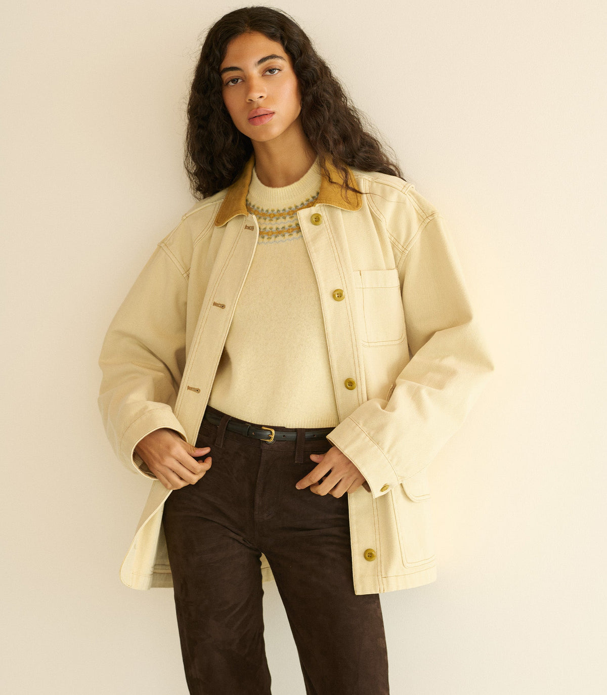 Woman wearing a light yellow barn jacket over a cream sweater and brown pants, standing against a plain background.