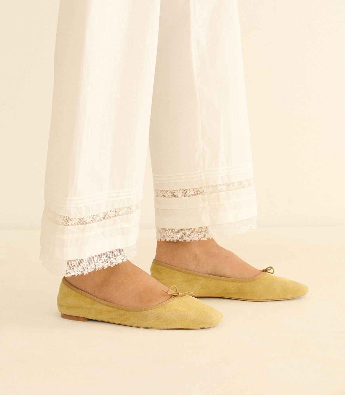 Yellow flats worn with white pants against a neutral background