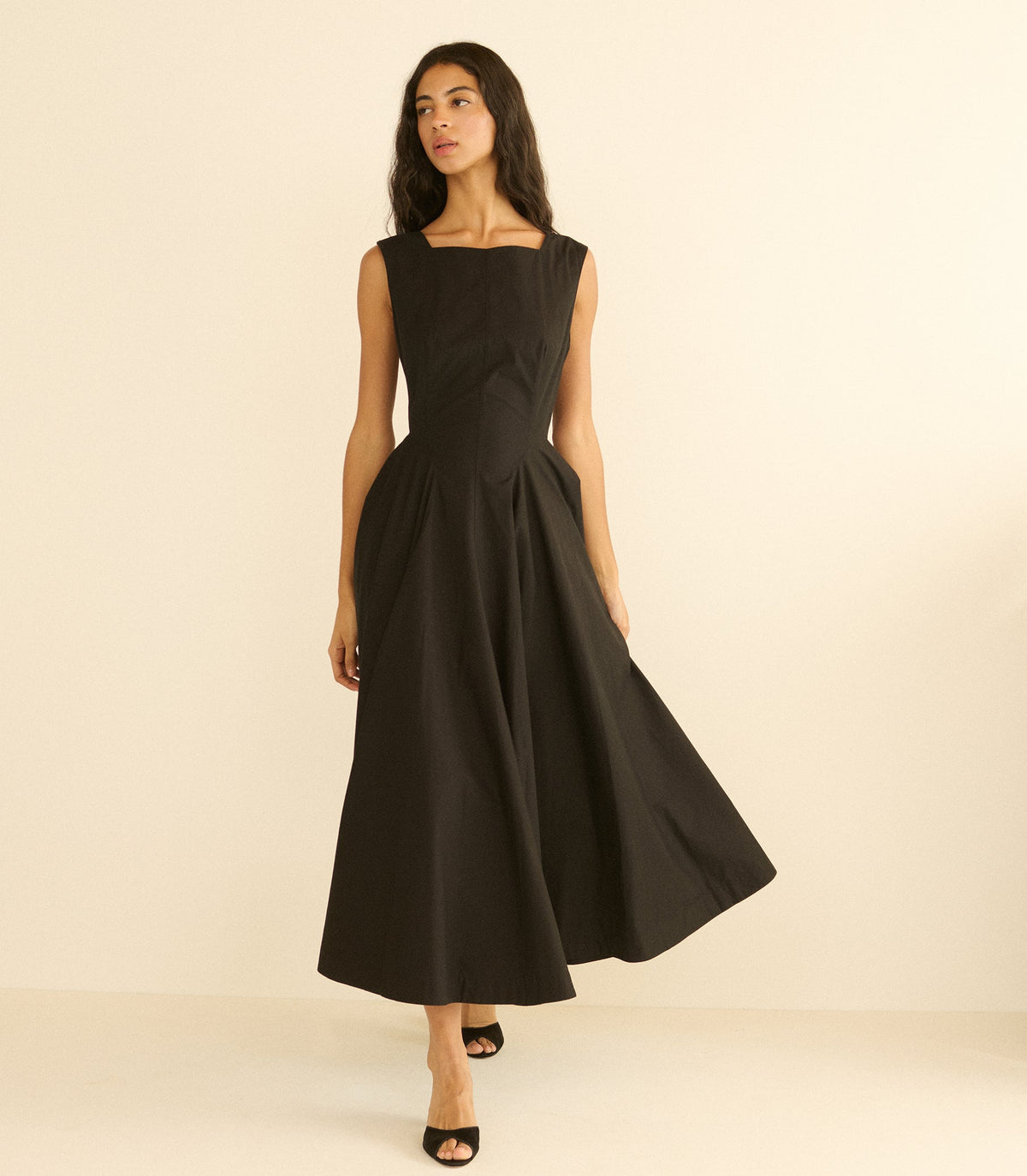 Woman wearing a long black dress against a beige background