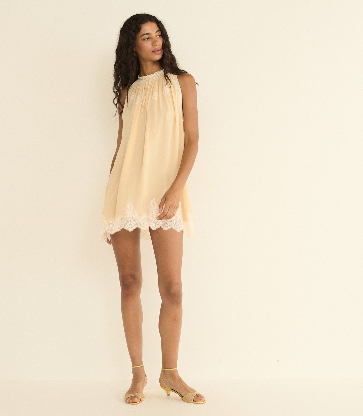 Woman wearing a light beige dress with lace trim on a plain background