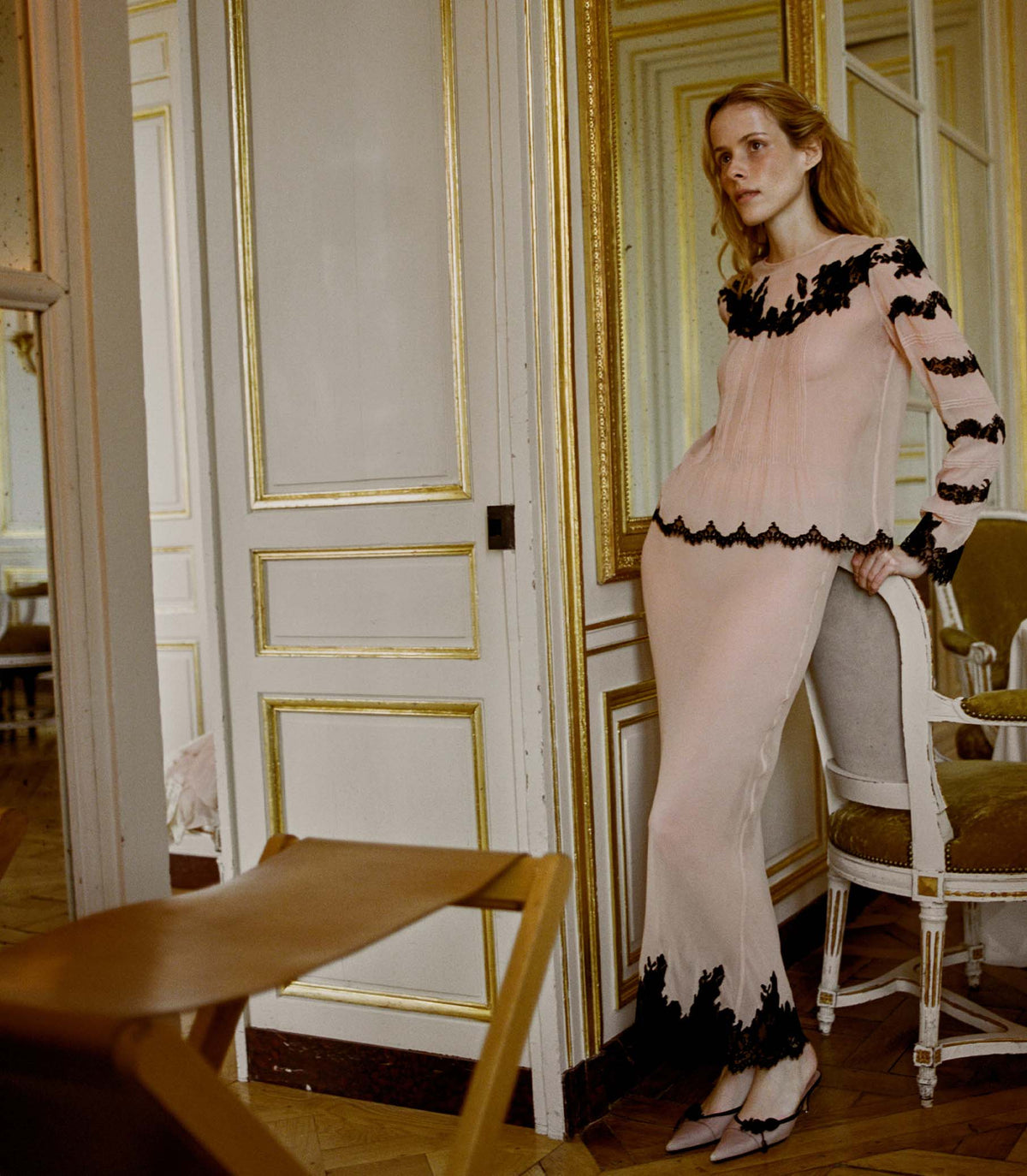 Woman in a peach & black lace skirt standing in an elegant room with gold-framed doors.
