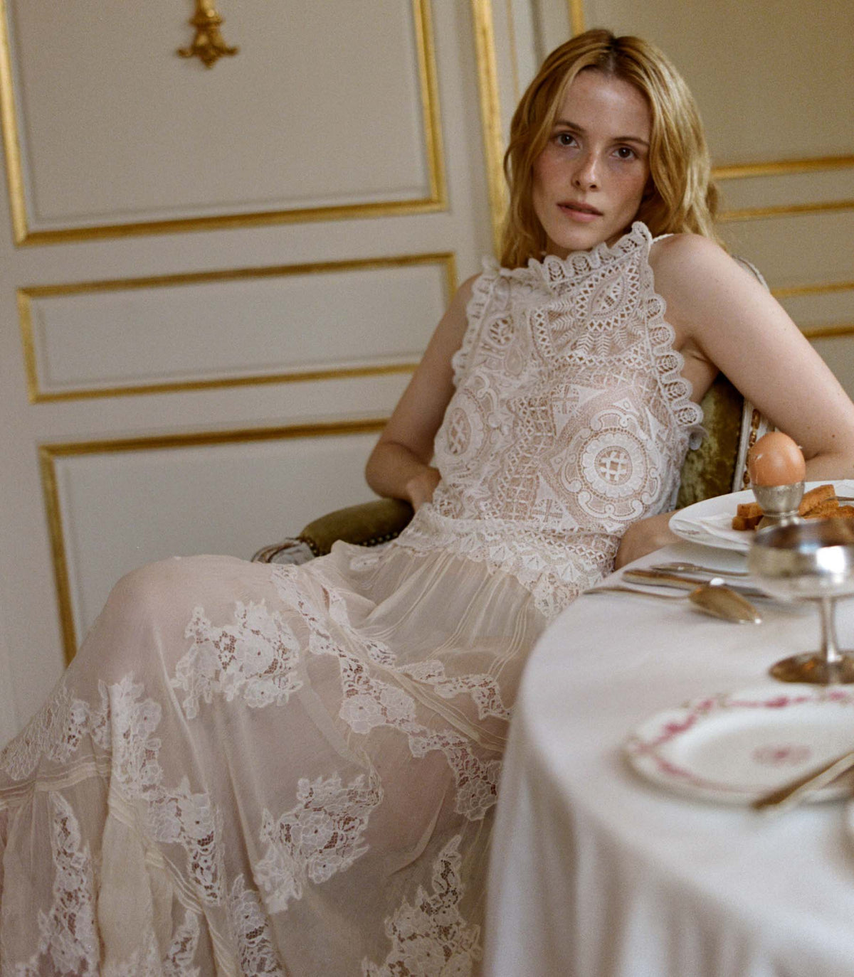 Woman wearing a white crochet lace top sitting at a table with a decorative setting.