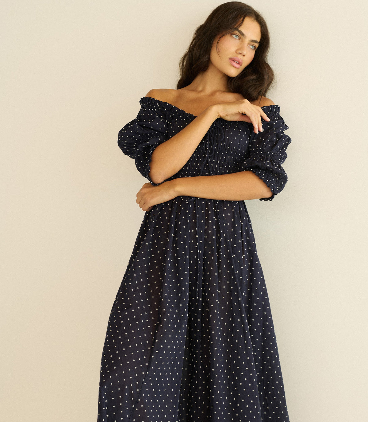 Woman wearing a navy blue dress with white polka dots against a beige background
