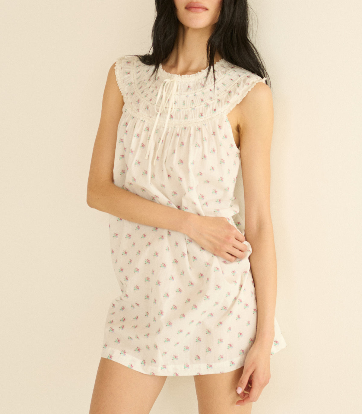 Woman wearing a white sleeveless dress with a subtle floral pattern on a plain background